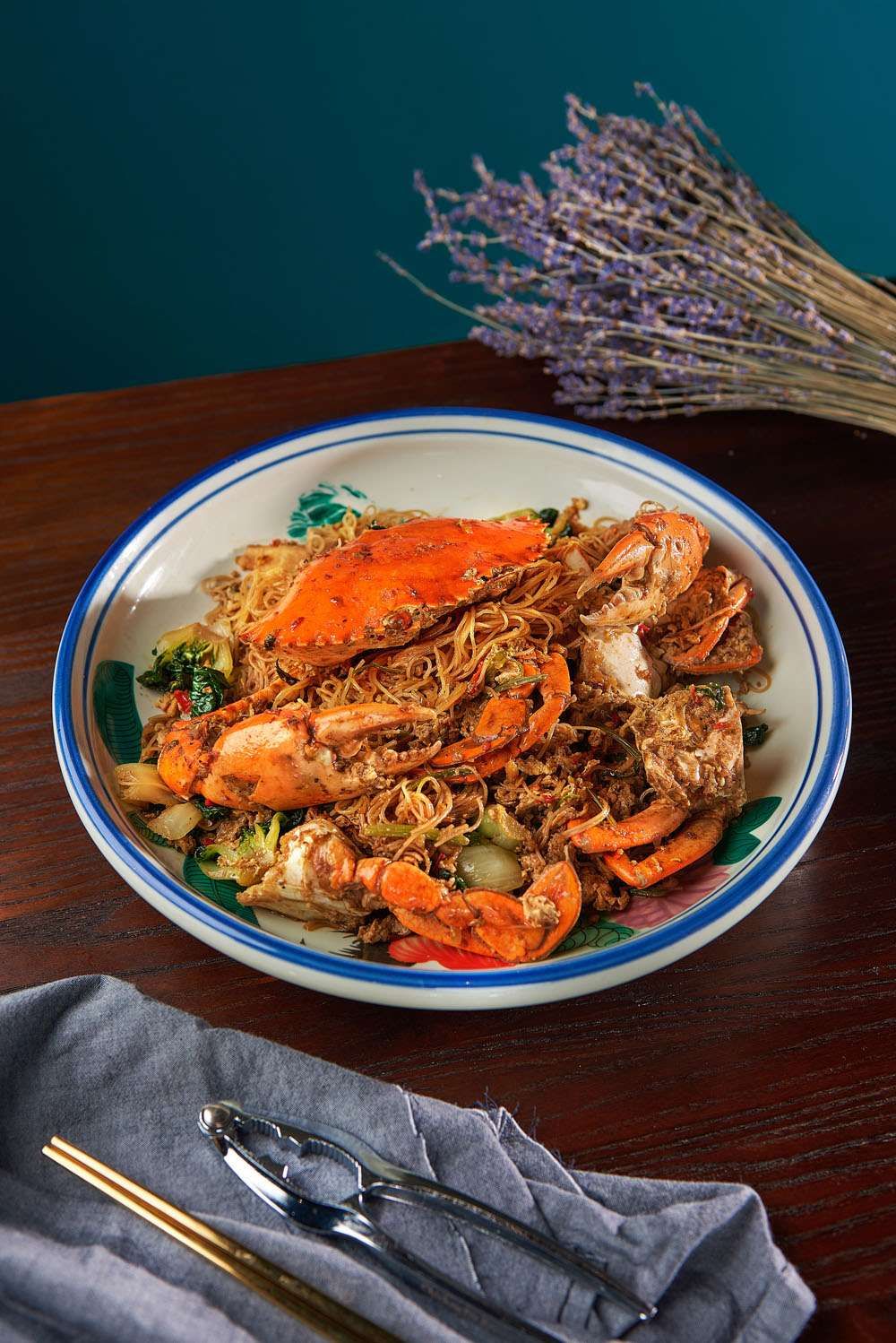 A whole crab on stir-fried bee hoon in a rich black pepper gravy, in a patterned bowl.