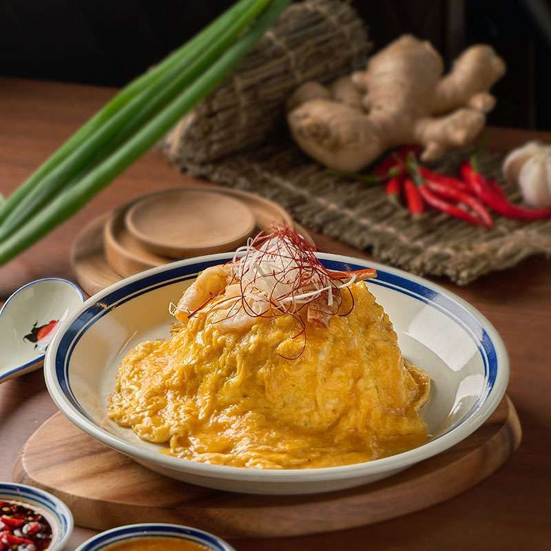 A plate of crab meat fried rice topped with a golden soft omelette, red threads of chilli and a garnish, in a blue-rimmed bowl.
