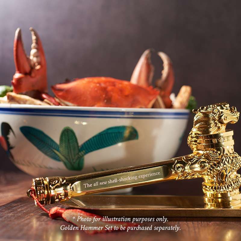 A whole crab in a blue-rimmed bowl beside a gold ornamental hammer, with a note that the photograph is for illustration only.