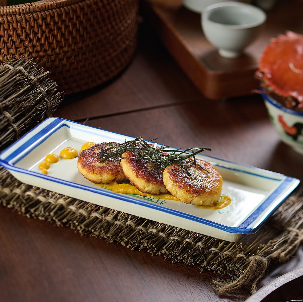 Three round Hokkaido crab cakes topped with strips of nori on a long white plate with blue rim.